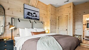 A wooden-paneled bedroom with a bed, bedside lamp, and a framed photograph on the wall. - Lakefront home with retro accents, private pool, and private dock. (Sevierville)