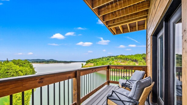 A wooden deck with outdoor seating overlooking a lake and forested hills. - Lakefront home with retro accents, private pool, and private dock. (Sevierville)