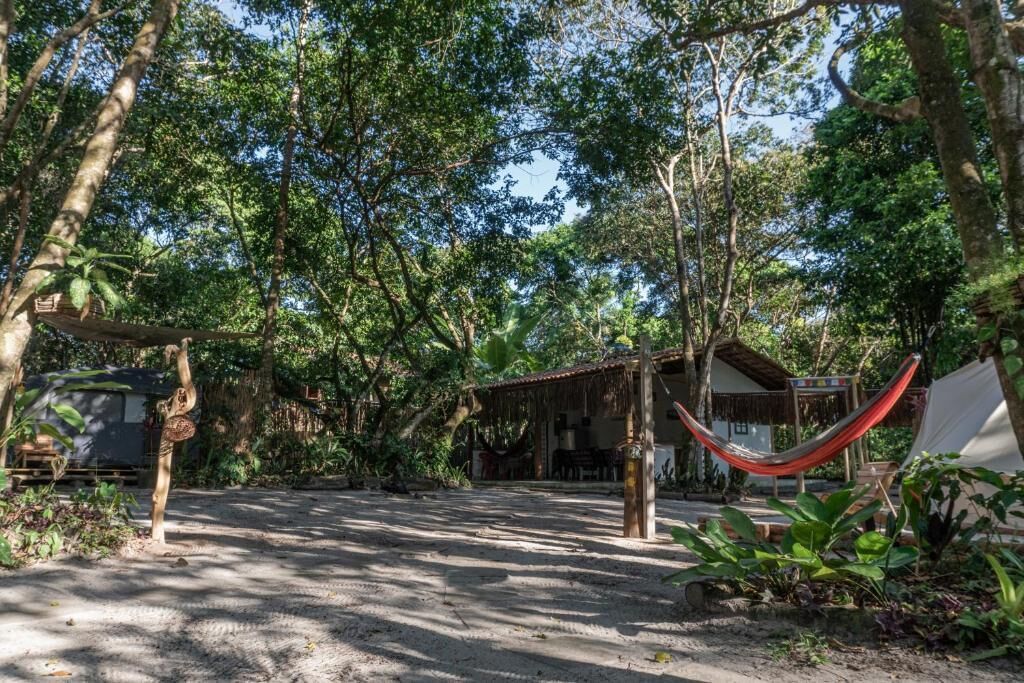 Un espacio al aire libre rústico con una hamaca, una estructura de techo de paja y un vehículo cerca.