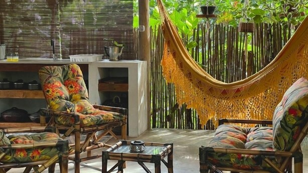 A room with a hammock, wicker furniture, and a bamboo backdrop. - Vila Coco Dendê (Maraú)