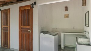 A laundry room with a washing machine, a sink, and wooden doors. - Vila Coco Dendê (Maraú)