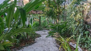 A narrow concrete pathway flanked by lush greenery and a white wall. - Vila Coco Dendê (Maraú)