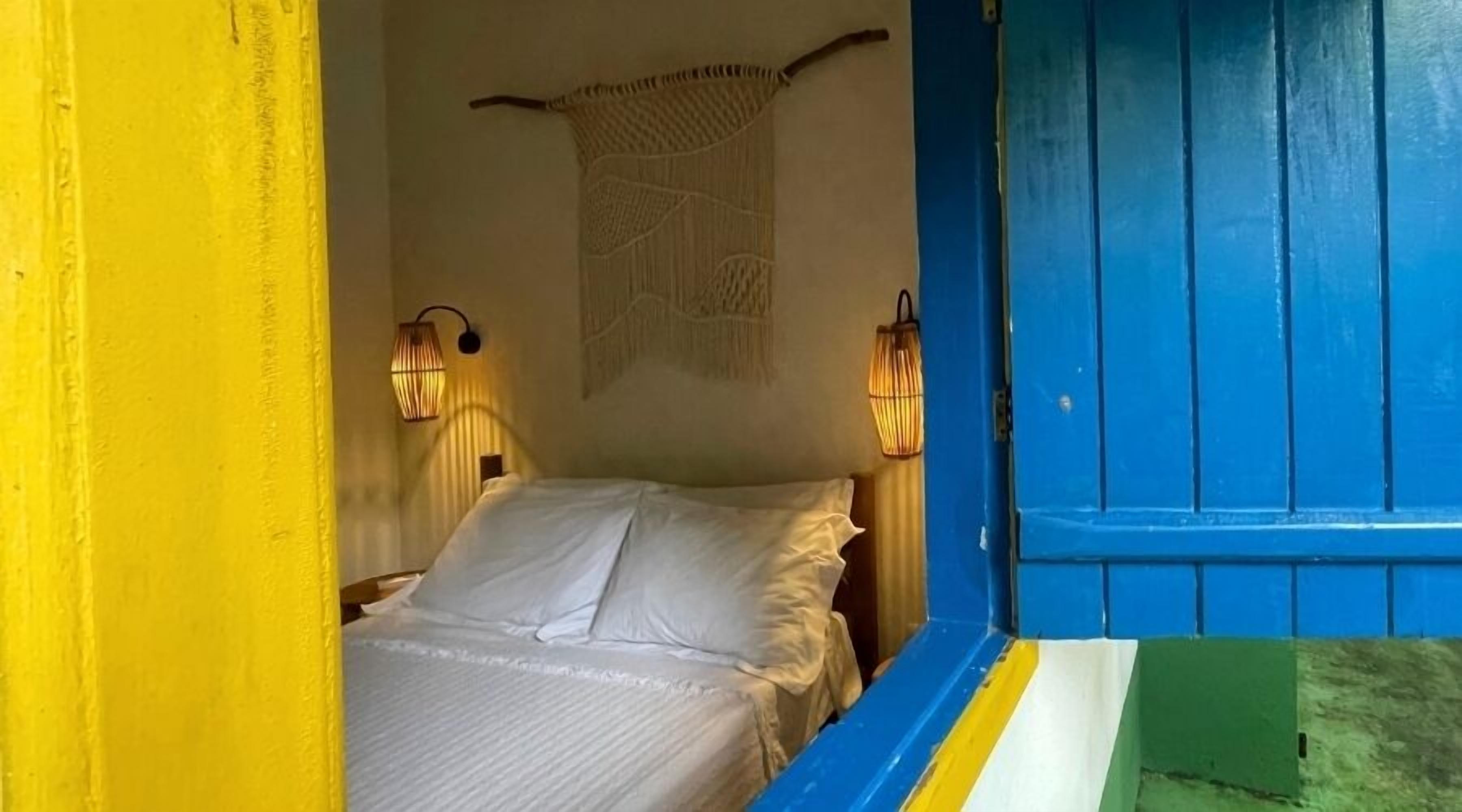 Una habitación con una cama, dos lámparas fijadas a la pared y una puerta azul.