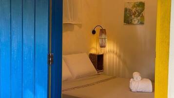 Un dormitorio con cama, una lámpara de noche, una toalla enrollada y un cuadro en la pared.
