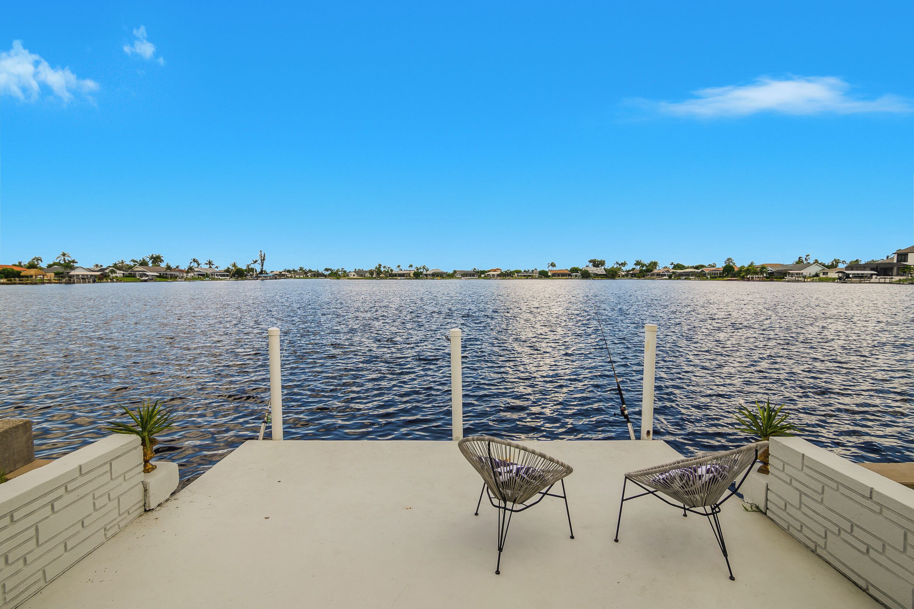 A waterfront patio with two wicker chairs, a concrete floor, and a view of the water and distant buildings.