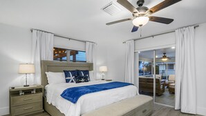 Ein Schlafzimmer mit Bett, Nachttischen, Deckenventilator und Blick durch eine Glastür.
