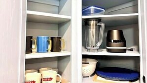 Een keuken met een blender, koffiezetapparaat en mokken op planken.