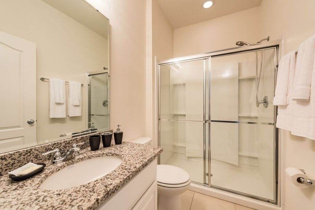 Een badkamer met een wastafelblad van graniet, een glazen douchecabine en een wit toilet.