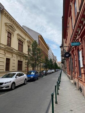 A street with parked cars and buildings, including a cafe with a visible sign.