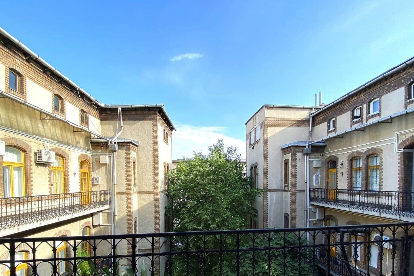Un patio con edificios de dos pisos, una cerca metálica y un árbol.