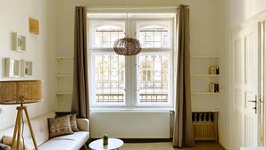 A room with a white sofa, a small round table, a hanging light fixture, and a window with curtains. - Superior Two-Bedroom Apartment (Budapest)