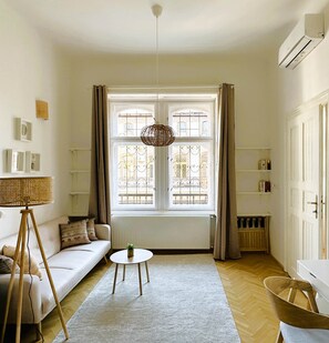 A room with a white sofa, a small round table, a hanging light fixture, and a window with curtains. - Superior Two-Bedroom Apartment (Budapest)