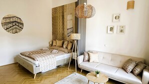 A modern bedroom with a bed, a sofa, a small round table, and a hanging lamp. - Superior Two-Bedroom Apartment (Budapest)