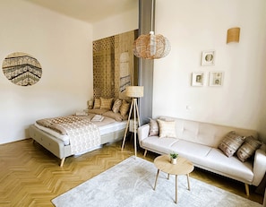 A modern bedroom with a bed, a sofa, a small round table, and a hanging lamp. - Superior Two-Bedroom Apartment (Budapest)