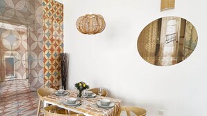 A dining area with a table set for four, a hanging light fixture, a wall-mounted mirror, and a patterned wall. - Superior Two-Bedroom Apartment (Budapest)