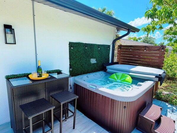 Ein Whirlpool mit einem blattformigen Sitz, ein kleiner Tisch mit einer Flasche und Gläsern sowie ein Korbstuhl.