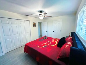 Ein Schlafzimmer mit einem Bett, einem Deckenventilator, weißen Türen und einem Fenster mit Jalousien.