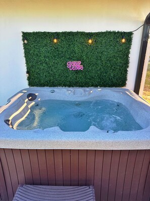 Ein Whirlpool mit Kunstgrasanlage im Grünton und einem Neon-Schild mit der Aufschrift 'Good Vibes'.