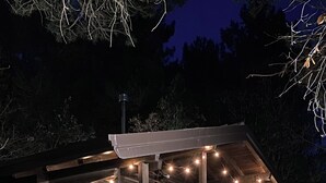 A log cabin with a covered porch and string lights, surrounded by a stone wall and leaf-covered ground. - Woods etna chalet (Sicilia)