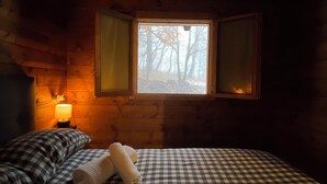 A cozy room with a checkered bedspread, a bedside lamp, and a window with a view of trees. - Woods etna chalet (Sicilia)