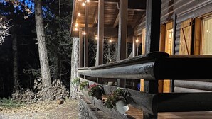 A rustic cabin with a stone foundation, wooden deck, and string lights. - Woods etna chalet (Sicilia)