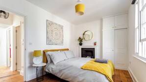 Un dormitorio con cama, una mesita, lámpara, espejo, chimenea y armario.
