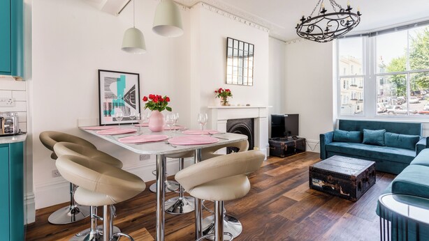 Una cocina moderna con comedor, taburetes de bar, chimenea y vista a la calle a través de amplios ventanales.