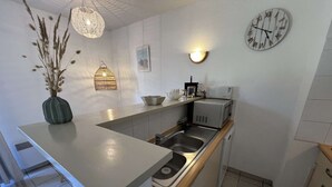 Kompakti keittiö, jossa on sisäänrakennettu pesuallas, mikroaaltouuni ja seinällä oleva kello.