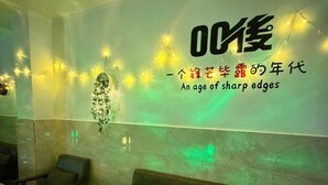Interno di un ristorante con un tavolo illuminato di verde, sedie e una parete decorata con luci a stringa e scritte.