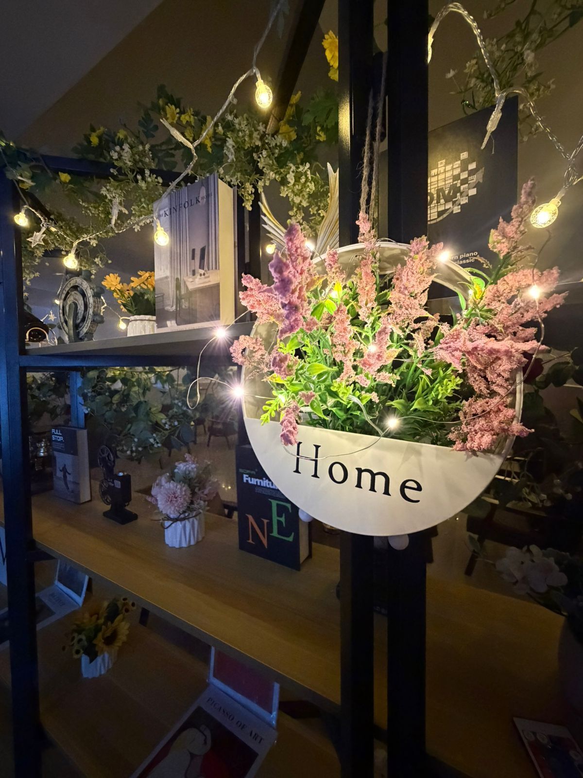 A hanging planter with the word 'Home' on it, surrounded by various decorative items and a bookshelf.