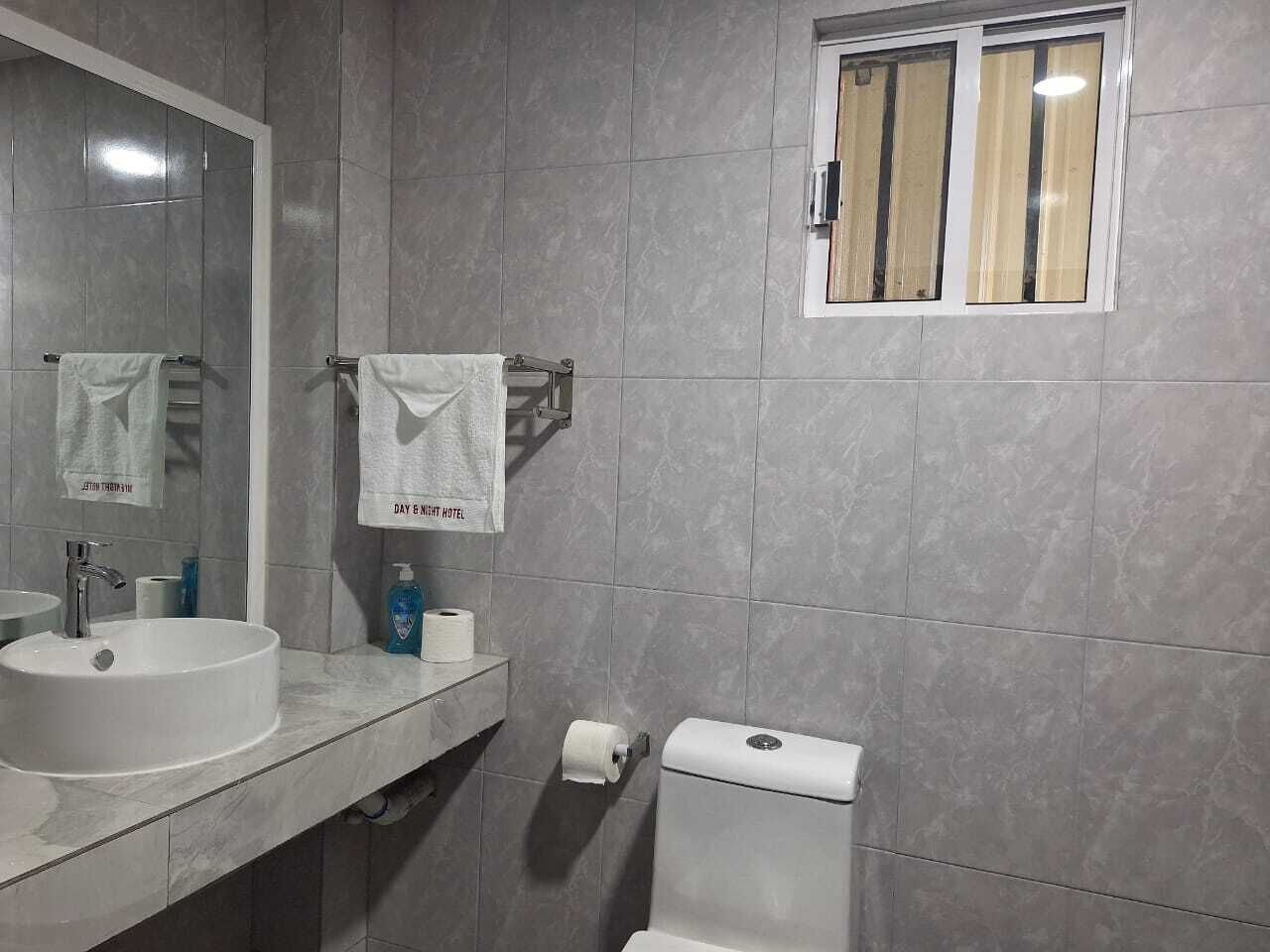 A bathroom with a white sink, a mirror, a towel rack, a toilet, and a window with curtains.
