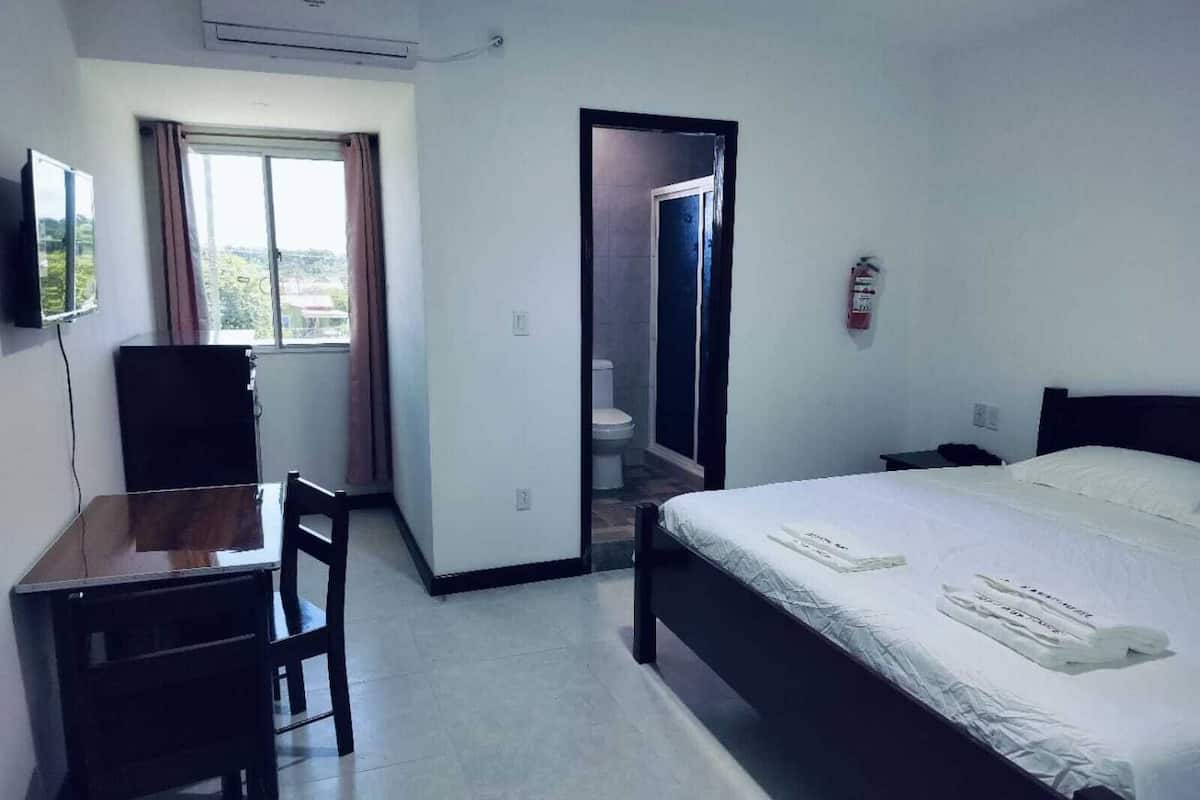 Habitación de hotel con cama, escritorio, silla, ventana con cortinas y puerta que da a un baño.