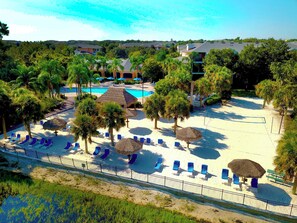 A resort with a pool, sun loungers, palm trees, and a fenced beach area.
