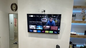 A living room with a mounted TV displaying a streaming service interface, a clock on the wall, and a wooden floor. - Fresh Apartment & Parking (London)