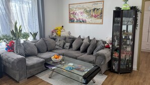 A modern living room with a grey sectional sofa, a glass coffee table, and a decorative glass cabinet. - Fresh Apartment & Parking (London)