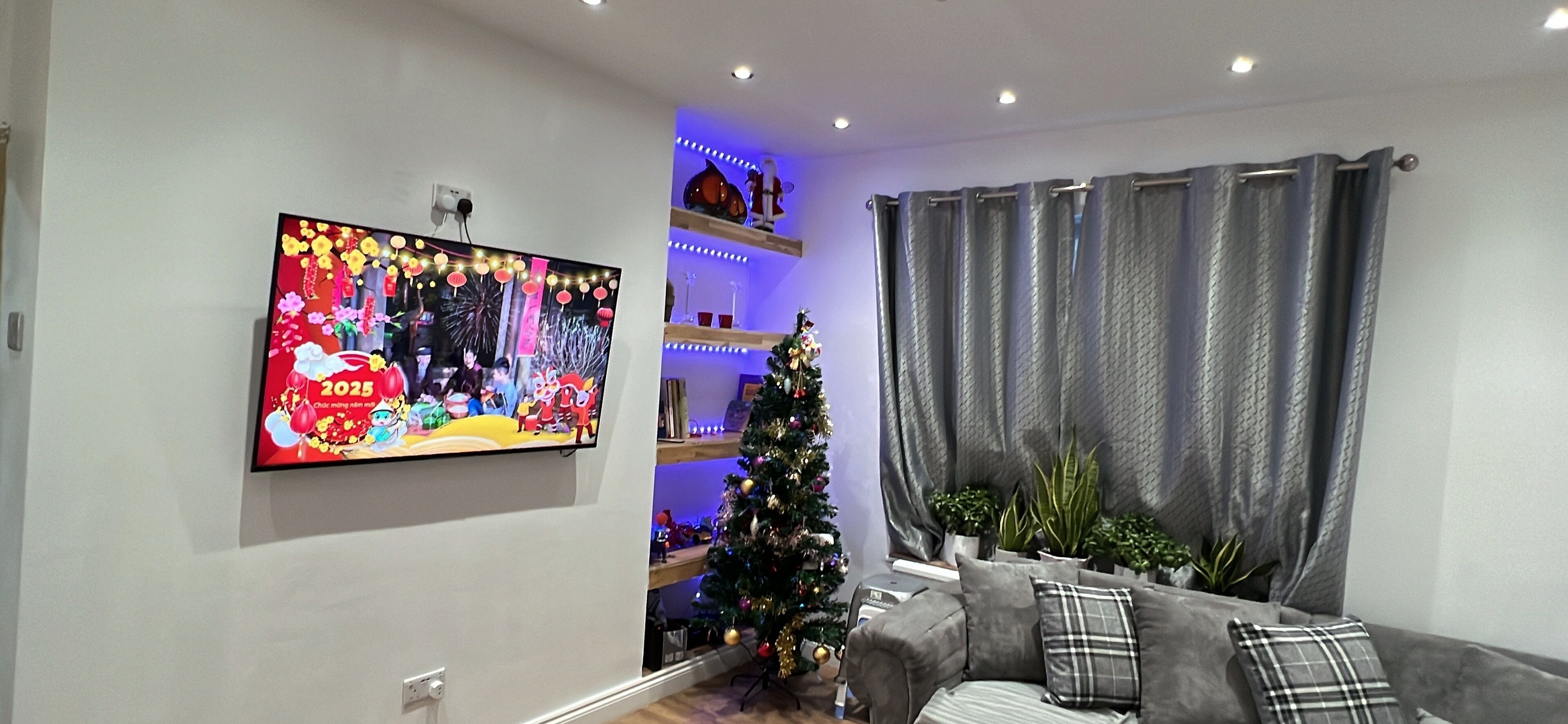 Ein Wohnzimmer mit Flachbildfernseher, Weihnachtsbaum und grauem Sofa.