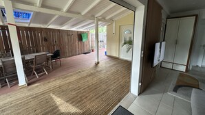 A covered outdoor area with a wooden deck, a table and chairs, and a door leading to a room with a wardrobe. - Residence La Terrasse (POINTE NOIRE)