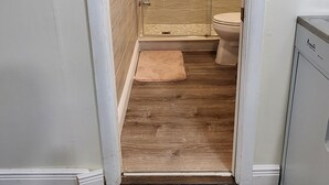 Kapea käytävä johtaa kylpyhuoneeseen, jossa on suihku, wc ja pieni matto lattialla.