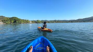 Vista desde un kayak sobre aguas tranquilas, con una persona remando a lo lejos.