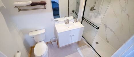 A bathroom with a toilet, a sink with a mirror, and a shower area.