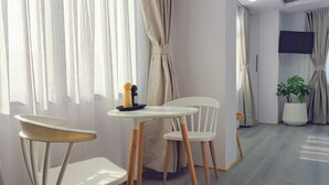 Ein modernes Zimmer mit Essbereich, ausgestattet mit zwei weißen Stühlen, einem kleinen Tisch, einer Zimmerpflanze und einem flachbildfernseher an der Wand.