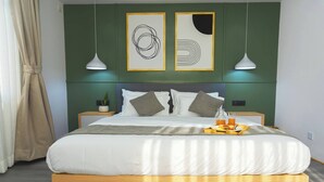 Ein ordentlich bezogenes Bett mit einem Frühstücksbrett, einer Topfpflanze und zwei gerahmten abstrakten Kunstwerken an der Wand.