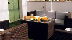 Ein gemütlicher Sitzbereich im Freien mit Korbmöbeln und einem Glastisch, gedeckt mit Frühstücksleckereien.