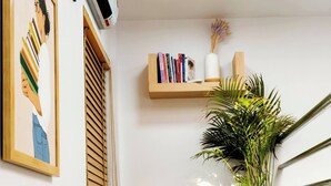 Ein modernes Interieur mit einem grauen Sitzsack auf einer Holztreppe, einer Wand-Klimaanlage, einem gerahmten Bild, einer Topfpflanze und einem Regal mit Büchern und Dekoartikeln.