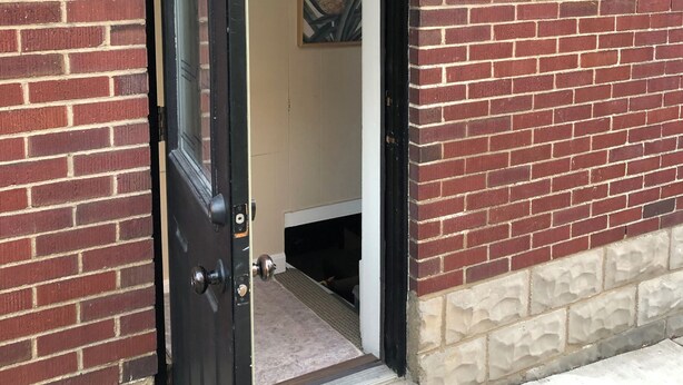 Un edificio de ladrillo con una puerta negra, un escalón que lleva a la entrada y un pequeño aplique en la pared.