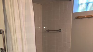 Un baño con una bañera, cortina de ducha, toallero, un estante pequeño y un cubo de basura.