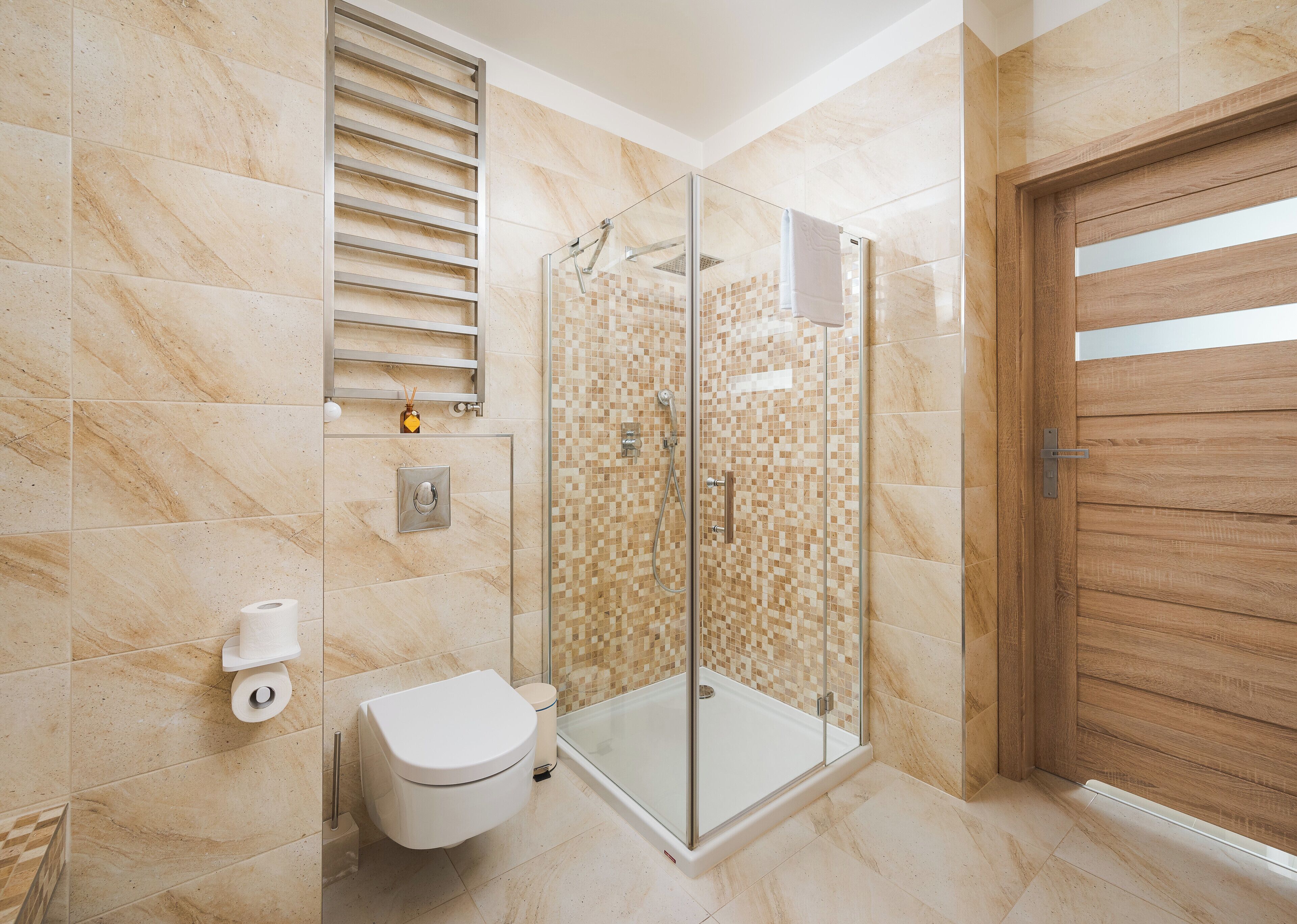 A modern bathroom with a glass-enclosed shower, a toilet, and a wooden door.