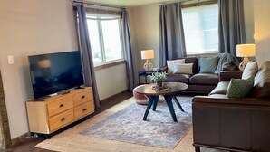Una sala de estar con una televisión de pantalla plana, un sofá, una mesa de centro y dos lámparas.