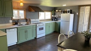 Una cocina con gabinetes verdes, estufa, fregadero, microondas y refrigerador. Hay una mesa de comedor con sillas.