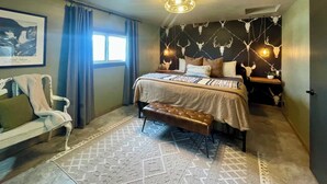Un dormitorio con cama, un banco, una silla, un tapete estampado y una pared decorada con calaveras.